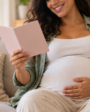 Gestante sorrindo em sala de estar clara com carteira de pre-natal